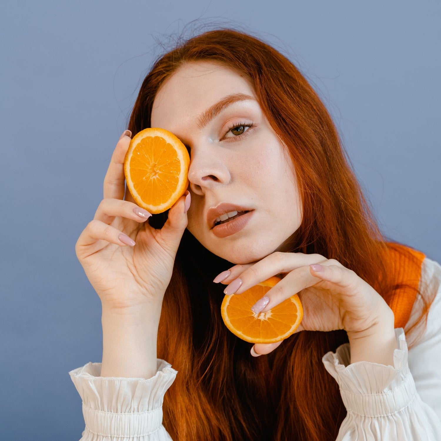 Woman holding orange slices to her face, vitamin C skincare