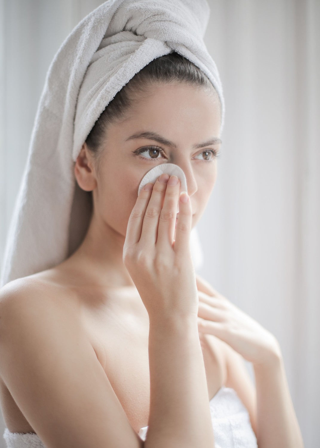 Woman in a towel wiping her face with a cotton pad, a face toner routine